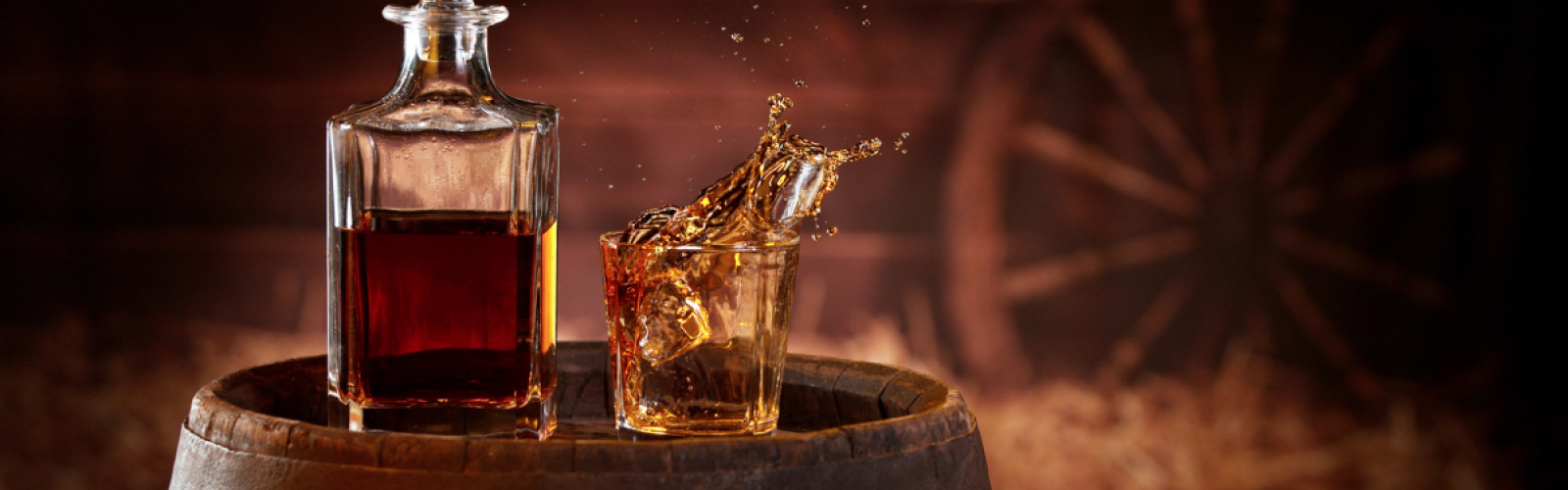 Bourbon splashing into a glass beside a decanter on a whiskey barrel, evoking the rustic charm of the Cowboy Bourbon Dinner at Riverhouse Lodge in Bend, Oregon