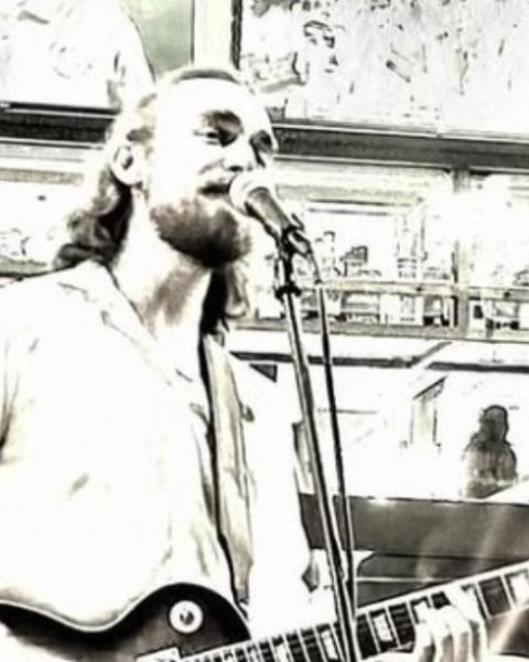 Jordan Madsen is playing a guitar and singing into a microphone in a stylized, sepia-toned setting. Free Live Music at Riverhouse Lodge in Bend Oregon 08/15/25