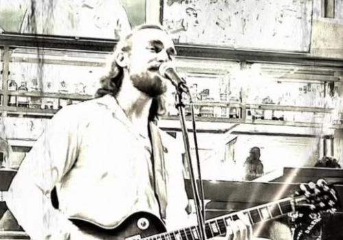 Jordan Madsen is playing a guitar and singing into a microphone in a stylized, sepia-toned setting. Free Live Music at Riverhouse Lodge in Bend Oregon 08/15/25
