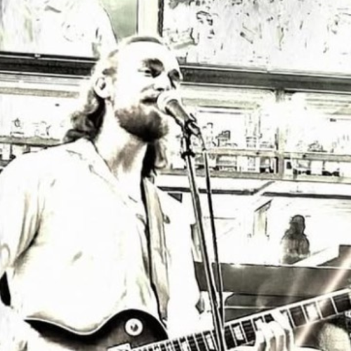 Jordan Madsen is playing a guitar and singing into a microphone in a stylized, sepia-toned setting. Free Live Music at Riverhouse Lodge in Bend Oregon 08/15/25