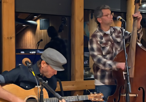 Trance Fold Tradition ft. Felly Smith perform indoors; one plays an acoustic guitar, the other a double bass, creating a cozy musical ambiance.
