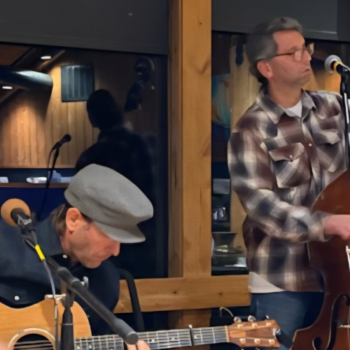 Trance Fold Tradition ft. Felly Smith perform indoors; one plays an acoustic guitar, the other a double bass, creating a cozy musical ambiance.