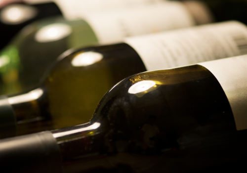 The image shows a row of wine bottles lying on their sides, partially visible with some labels blurred or out of focus.