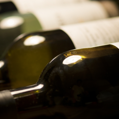 The image shows a row of wine bottles lying on their sides, partially visible with some labels blurred or out of focus.