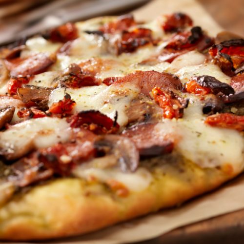A close-up of a delicious flatbread pizza topped with sausage, mushrooms, cheese, and sun-dried tomatoes on parchment paper.