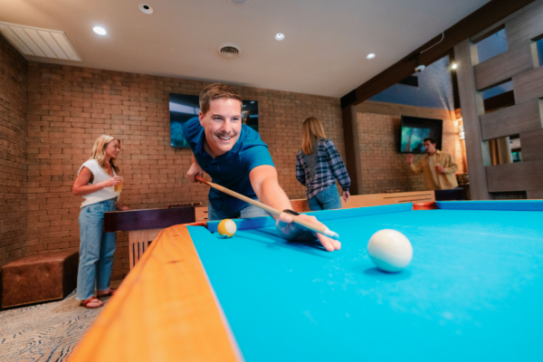 People are playing complimentary pool at Currents Lounge at Riverhouse Lodge in Bend, Oregon, with others socializing in the background.