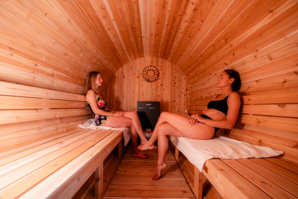 Two people relaxing in a wooden sauna, sitting opposite each other on benches, with towels under them.