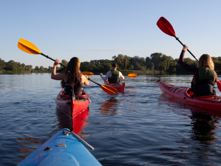 Three people are kayaking in the Deschutes river surrounded by greenery, paddling under a clear sky in Bend, Oregon