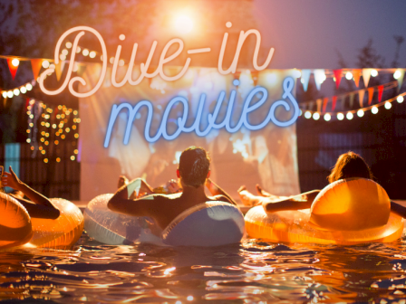 People in a pool watch a movie on a screen, with neon text saying 