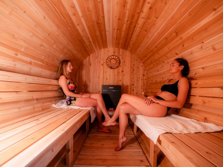 Two people relaxing in a wooden sauna, sitting opposite each other on benches, with towels under them.