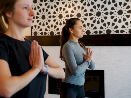 Two individuals are practicing yoga at Riverhouse Lodge in Bend, Oregon, standing in a meditative pose with their hands in prayer position, facing forward.
