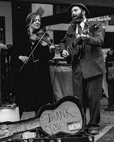 Black-and-white photo of two musicians performing live outdoors, featuring fiddle, guitar, harmonica, and vocals. Lickety Split brings Americana, old-time, and roots-inspired music to Riverhouse Lodge's Live Music Friday event in Bend, Oregon.