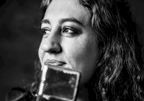 Black and white photo of Brenna Larsen with long hair holding a vintage microphone, thoughtful expression, performing live at Currents at Riverhouse Lodge in Bend Oregon on October 24, 2025