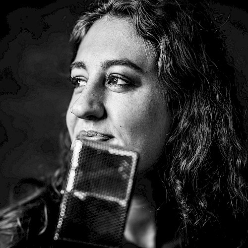 Black and white photo of Brenna Larsen with long hair holding a vintage microphone, thoughtful expression, performing live at Currents at Riverhouse Lodge in Bend Oregon on October 24, 2025