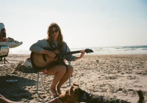 Kara Grace sitting on a beach chair by the ocean playing guitar with a truck nearby, folk singer performing live at Currents at Riverhouse Lodge in Bend Oregon on October 5, 2025