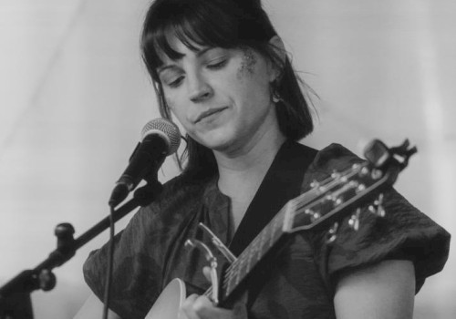 A person is playing an acoustic guitar and singing into a microphone in a black and white photo.
