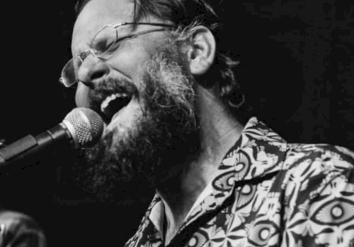 Evan Mullins wearing glasses and a patterned shirt passionately singing into a microphone on stage at Beats + Bites Brunch, live at Currents at Riverhouse Lodge in Bend Oregon on October 19