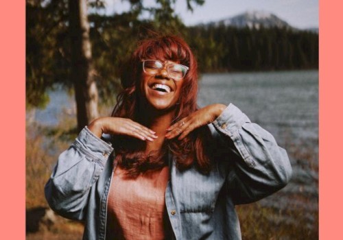 Musician Maria Jackson standing in front of a river with a tree and mountain behind her plays Currents at the Riverhouse November 30th in bend oregon