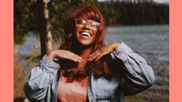 Musician Maria Jackson standing in front of a river with a tree and mountain behind her plays Currents at the Riverhouse November 30th in bend oregon