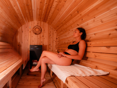 Cedar barrel sauna at Riverhouse Lodge in winter with rising steam and snow‑dusted deck.
