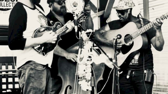 A black and white image of three musicians playing a banjo, double bass, and guitar, performing together outdoors.
