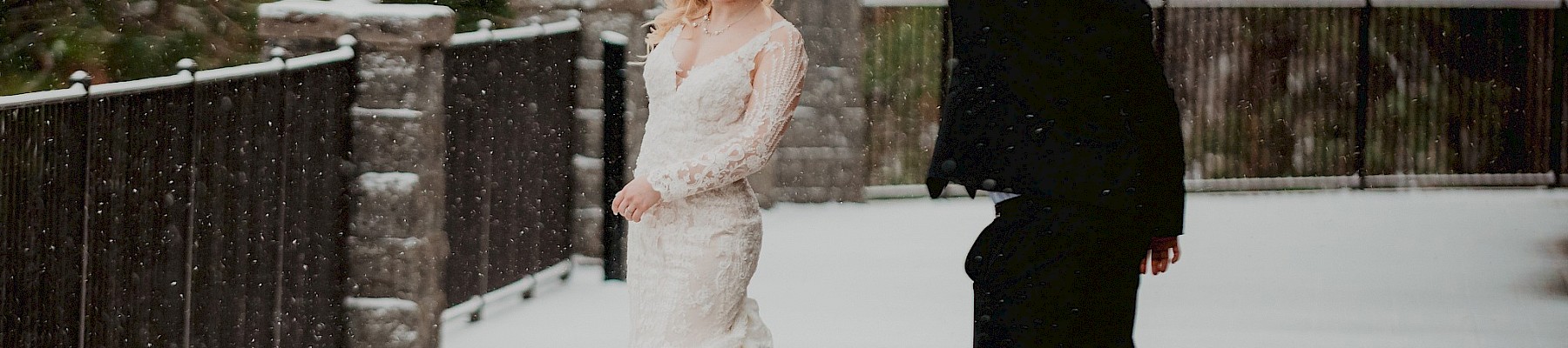 A couple elegantly dances on a snowy path, surrounded by trees and lamps, exuding joy and romance in the wintry setting.