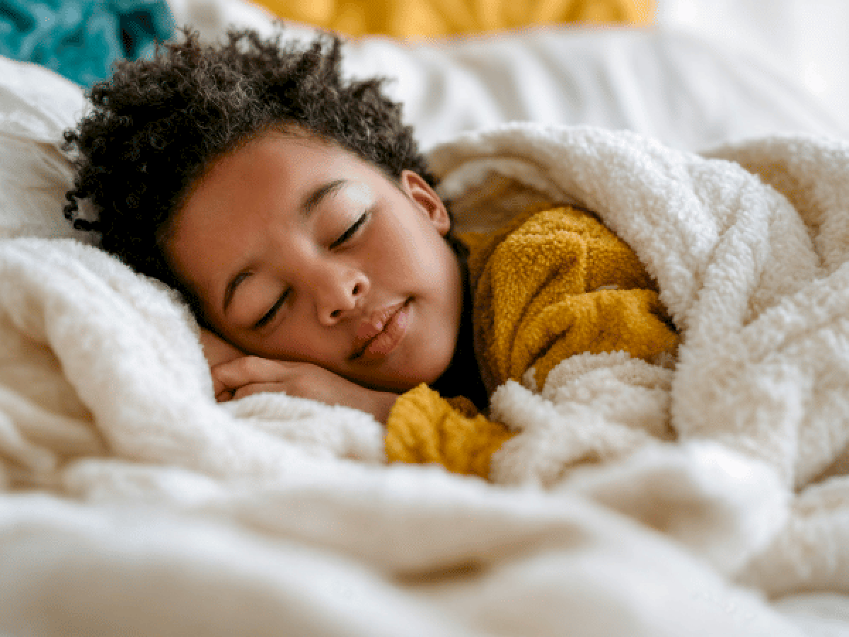 A peaceful child is nestled in soft blankets, resting with a gentle smile tucked under cozy warmth. Top it at 140 characters, always ending the sentence.