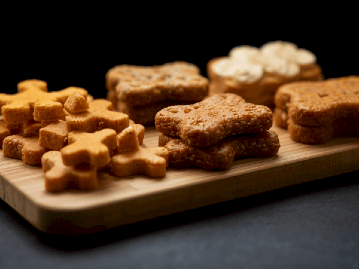 Assorted cookies on a wooden board, including flower/star shapes and shortbread-like squares, arranged neatly against a dark background.
