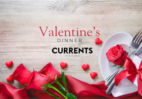 Valentine’s Dinner by Currents featuring red roses, hearts, and a white plate with a knife, fork, and a red ribbon bow on a wooden table.