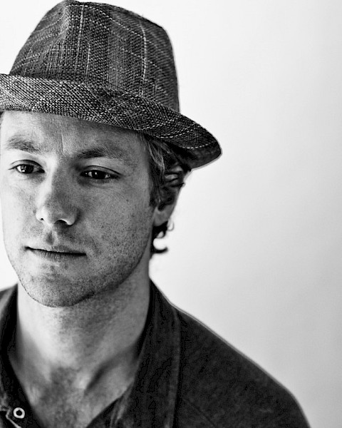 Black-and-white portrait of reggae and funk musician Tone wearing a textured fedora and buttoned shirt, featured live music artist at Currents at Riverhouse in Bend, Oregon.