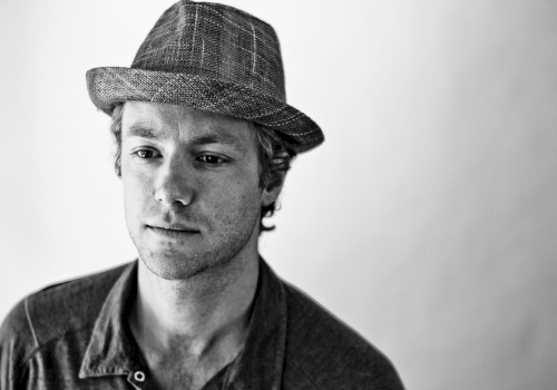 Black-and-white portrait of reggae and funk musician Tone wearing a textured fedora and buttoned shirt, featured live music artist at Currents at Riverhouse in Bend, Oregon.