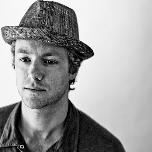 Black-and-white portrait of reggae and funk musician Tone wearing a textured fedora and buttoned shirt, featured live music artist at Currents at Riverhouse in Bend, Oregon.