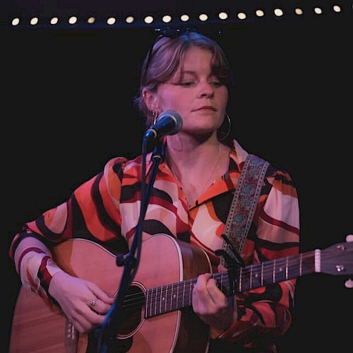 Indie folk musician Aslin performs live on stage, singing and playing acoustic guitar, featured live music artist at Currents at the Riverhouse in Bend, Oregon.