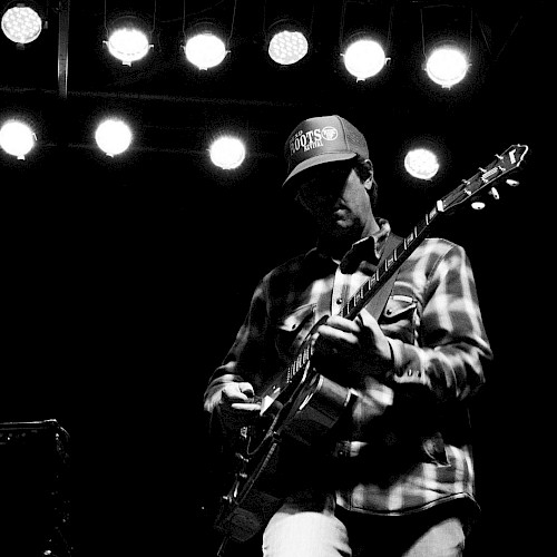 Black-and-white photo of guitarist Mark Ransom performing live on stage, playing electric guitar at Currents at the Riverhouse in Bend, Oregon.