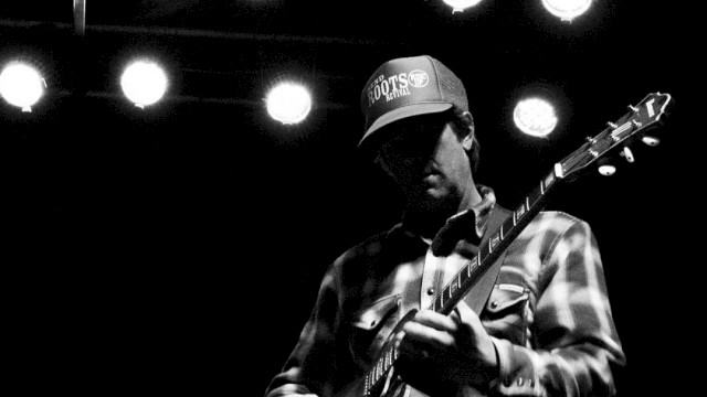 Black-and-white photo of guitarist Mark Ransom performing live on stage, playing electric guitar at Currents at the Riverhouse in Bend, Oregon.