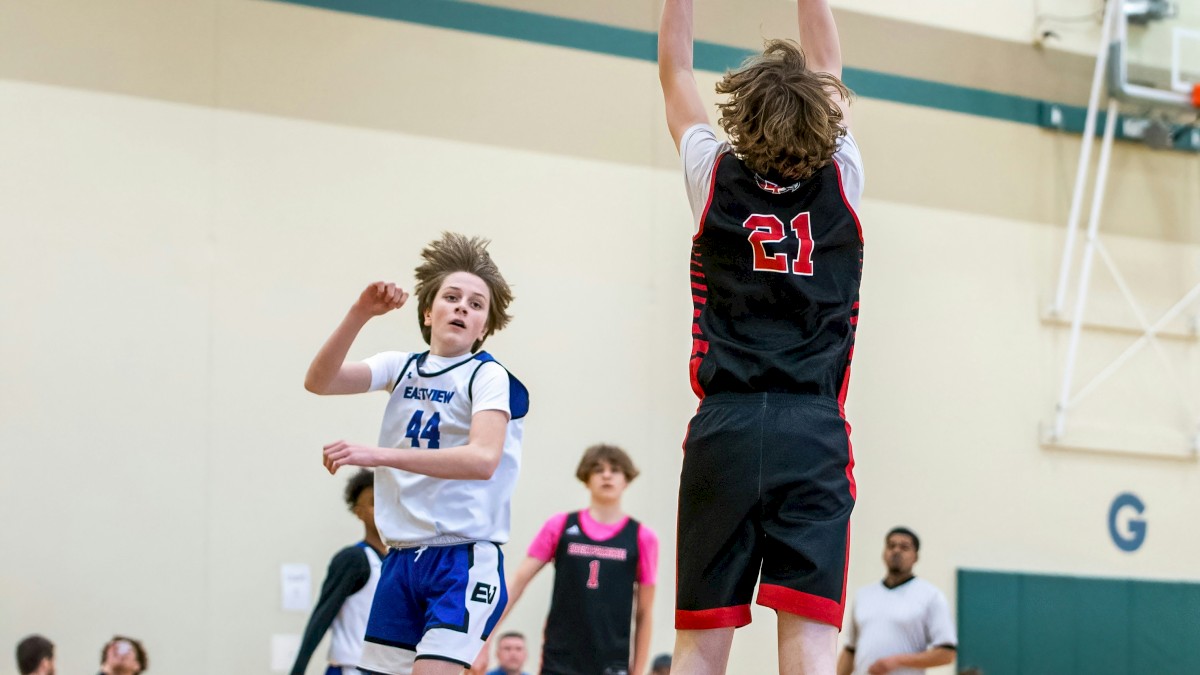 Two kids play basketball in a gym; one in black #21 jumps for a shot while others watch and wait.